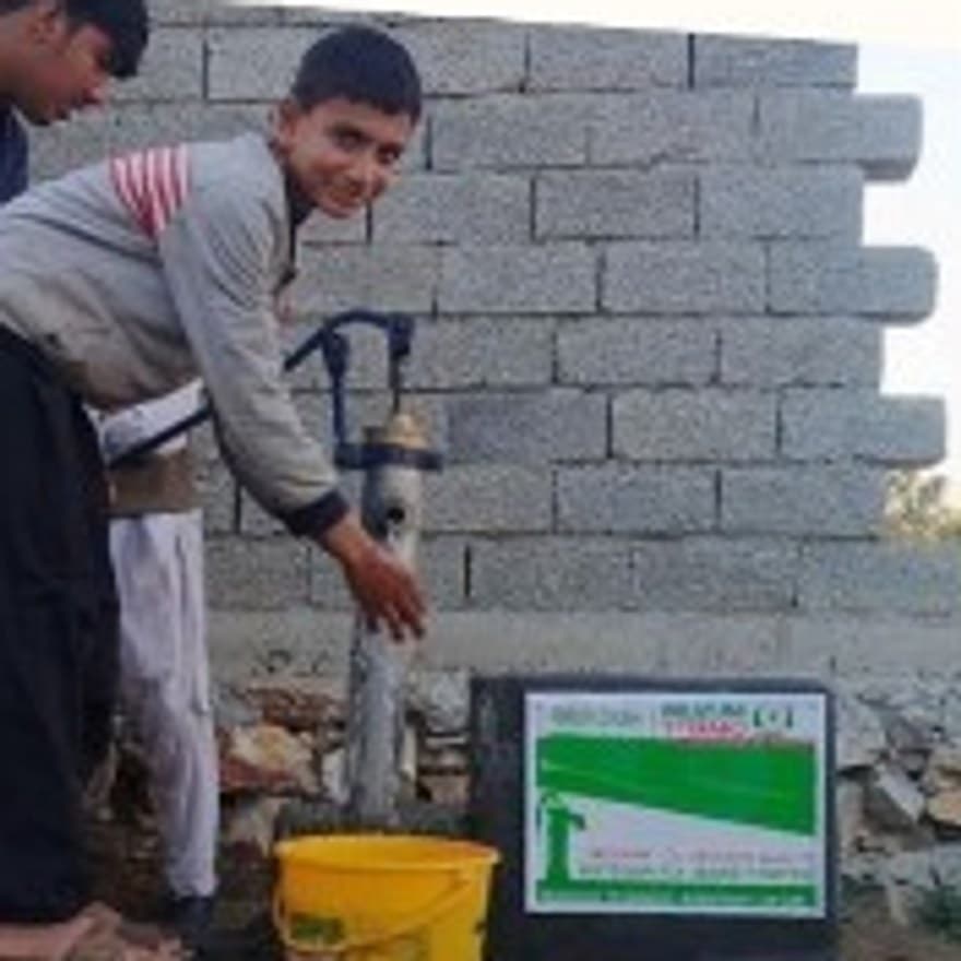 Two boys fill a bucket at a newly installed hand pump