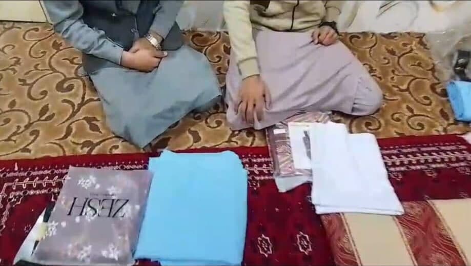 Two people kneel on a rug over folded fabric and a wrapped set of clothes ready to hand over